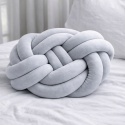 Jasnoszara poduszka dekoracyjna węzeł knot pillow na łóżku