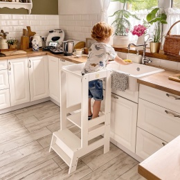 Dziecko stojące na białym kitchen helperze Montessori przy zlewie - bezpieczna wieża kuchenna do wspólnego gotowania