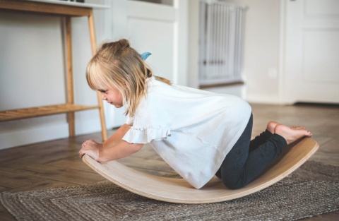 Dziewczynka ćwicząca równowagę na drewnianej desce balansowej Montessori