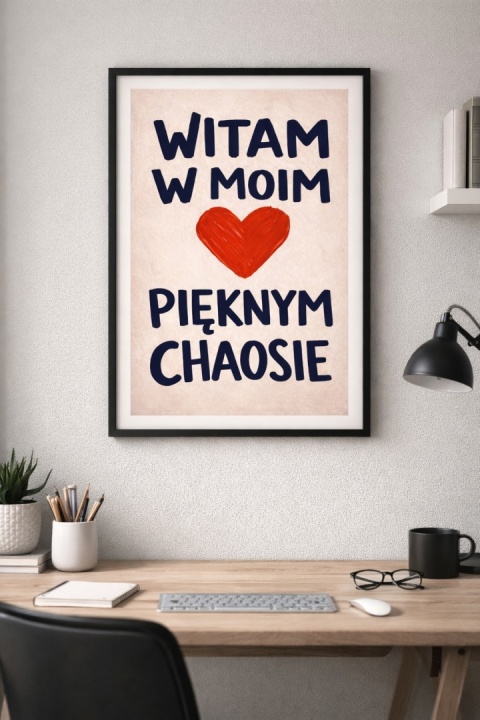 Plakat „Witam w moim pięknym chaosie” w czarnej ramie nad biurkiem w nowoczesnym biurze