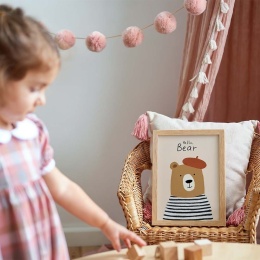 Ramka z plakatem misia Hello Bear w przytulnym pokoju dziecięcym, dekoracja na wiklinowym fotelu w pastelowej aranżacji