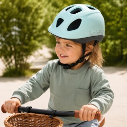 Dziewczynka w miętowym kasku dziecięcym Bobike GO podczas jazdy na rowerku biegowym w parku