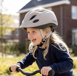 Dziewczynka w beżowym kasku dziecięcym Bobike podczas jazdy na rowerku