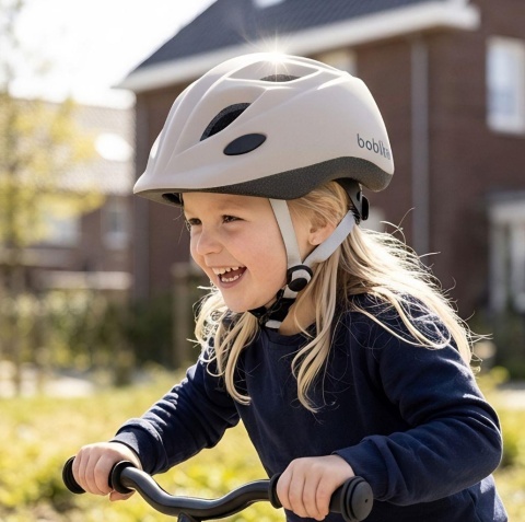 Dziewczynka w beżowym kasku dziecięcym Bobike podczas jazdy na rowerku