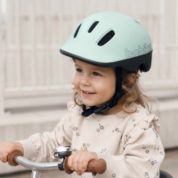 Dziecko w miętowym kasku rowerowym Bobike podczas jazdy na rowerku