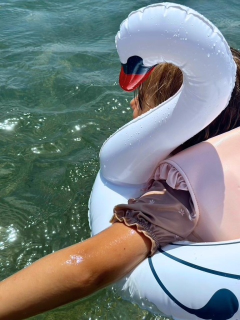 Dziecko w dmuchanym kole do pływania łabędź Vanilla Copenhagen podczas zabawy w wodzie na plaży