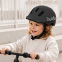 Dziecko w czarnym kasku rowerowym Bobike GO podczas jazdy na hulajnodze – lekki kask ochronny dla dzieci