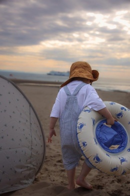Dziecko spacerujące po plaży z dmuchanym kołem do pływania Vanilla Copenhagen w niebieskie kraby.