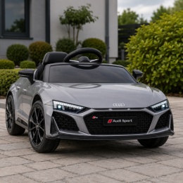 Srebrne Audi R8 na akumulator dla dziecka na podjeździe przed domem – sportowy samochód elektryczny z reflektorami LED