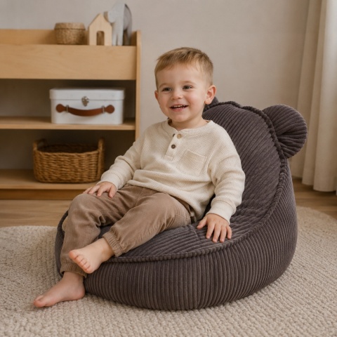 Dziecko siedzące na brązowej pufie dla dziecka Teddy Aesthetic w przytulnym pokoju dziecięcym
