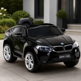 Czarne BMW X6M na akumulator dla dzieci przed nowoczesnym domem